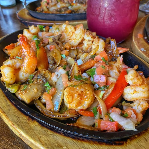 Sizzling shrimp fajitas with onions, peppers, and pico de gallo, alongside a pink drink.