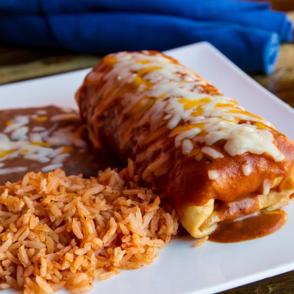 A Sonrisa Grill burrito covered in red sauce and melted cheese, served with rice and refried beans.
