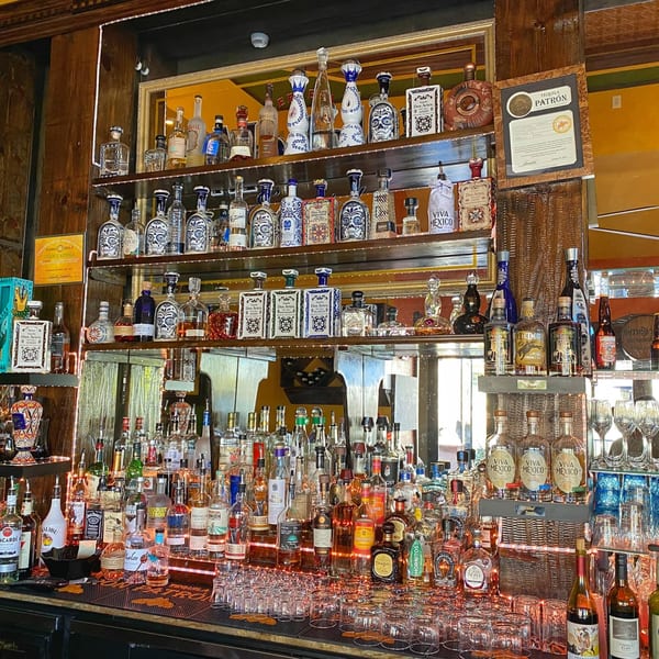 A well-stocked bar at Sonrisa Grill with numerous tequila bottles, including Patron, and glassware.