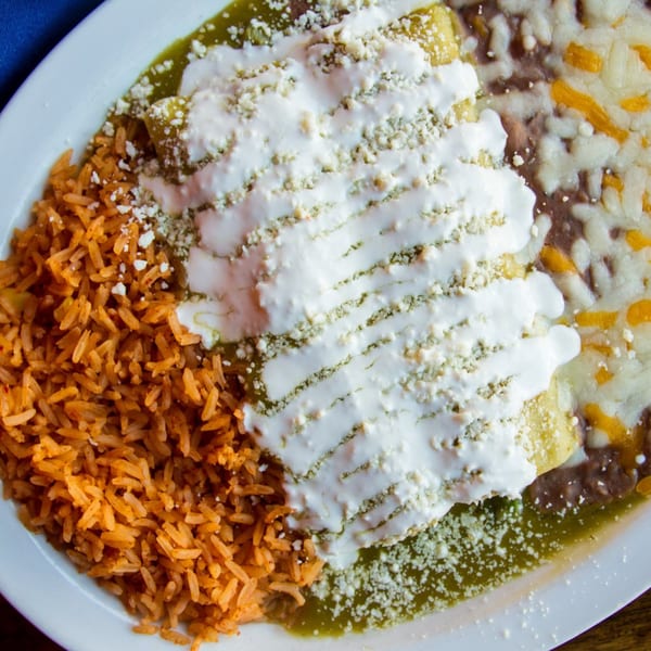 Sonrisa Grill's enchiladas with green sauce, sour cream, rice, and refried beans on a white plate.