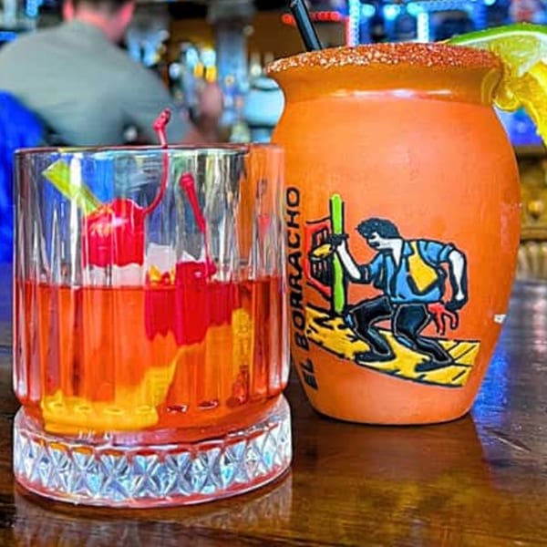 Two Sonrisa Grill cocktails, one in a glass with cherries, the other in an orange mug.
