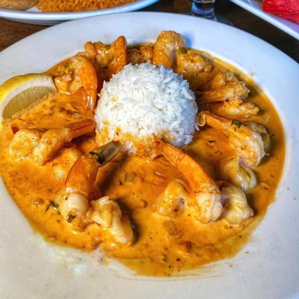 Shrimp in a rich orange sauce with a mound of white rice and a lemon wedge.