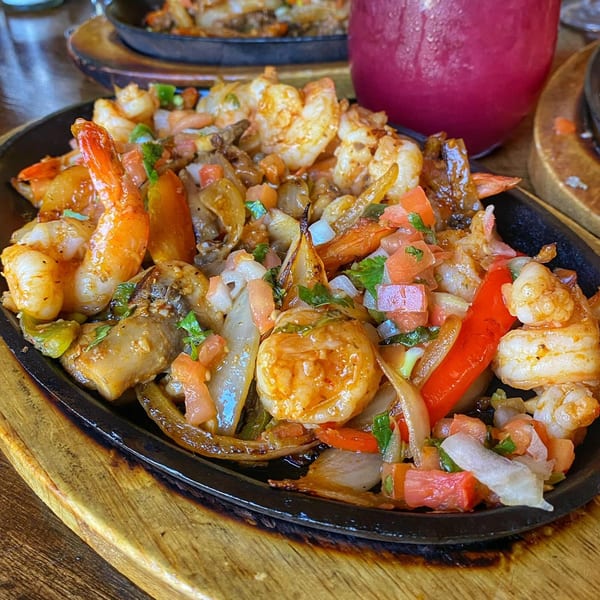 Sizzling shrimp fajitas with onions, peppers, and pico de gallo on a cast iron skillet.