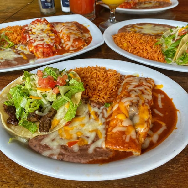 Three plates of Sonrisa Grill's Mexican food, including enchiladas, tacos, rice, and beans.