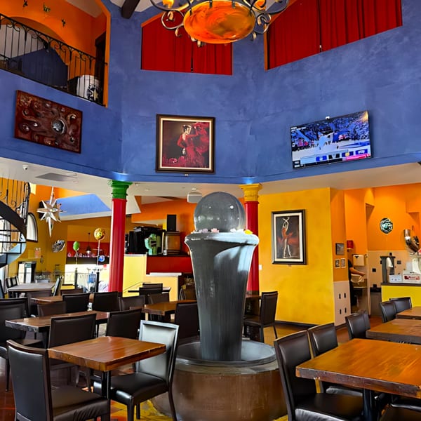 Colorful Sonrisa Grill dining room with blue and orange walls, dark tables, chairs, and a central fountain.