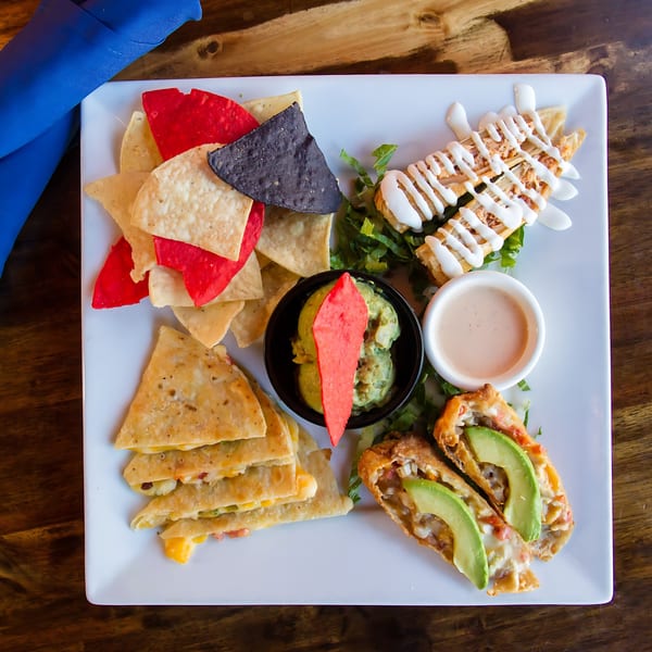 A white plate of Sonrisa Grill's Mexican appetizers, including nachos, quesadillas, taquitos, and egg rolls.