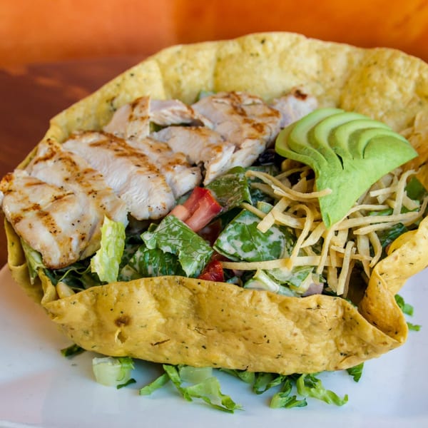 Sonrisa Grill's chicken taco salad with avocado slices, lettuce, and tomatoes in a crispy tortilla bowl.