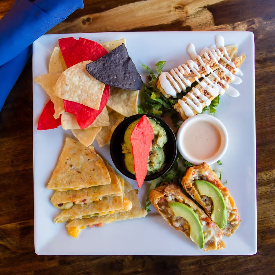 Mexican appetizer platter with quesadillas, taquitos, guacamole, chips, and avocado egg rolls.