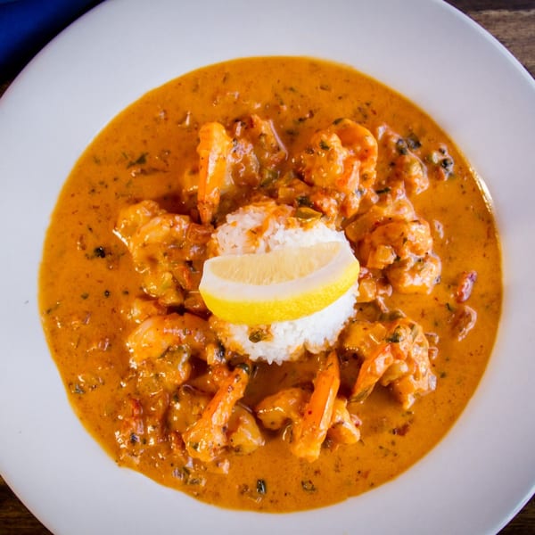 Shrimp in a rich orange sauce with white rice and a lemon wedge on a white plate.