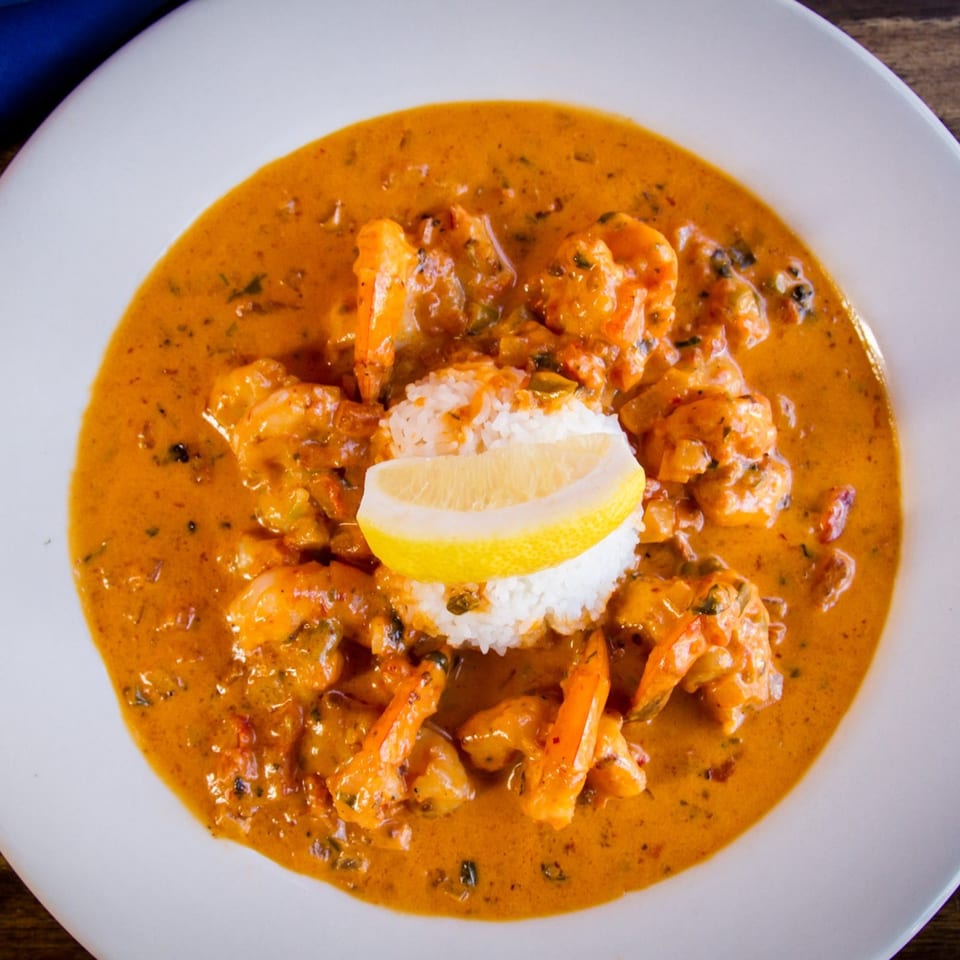 Shrimp in a rich orange sauce with white rice and a lemon wedge on a white plate.